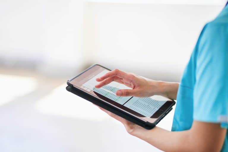 Medical professional in blue scrubs using a tablet to access digital health records