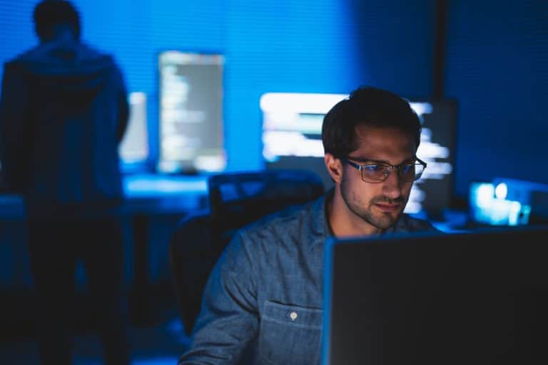 oftware developer working on laptop in dark room with multiple screens