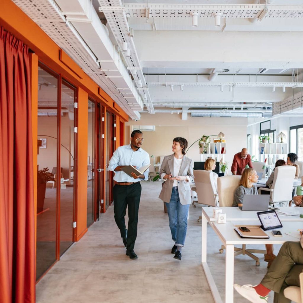 Two colleagues walking through a vibrant office with team members working at their desks